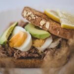 Close-up of a healthy avocado, tuna, and egg sandwich with lemon slices.