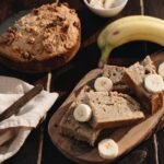 A rustic presentation of homemade banana bread with fresh bananas on a wooden board.