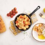 Delicious Italian pasta in a skillet with fresh ingredients and rustic bread.