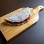 A flavorful tapioca wrap filled with ingredients displayed on a wooden board.