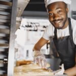 Cheerful male baker showcasing freshly baked baguettes in a bakery setting.
