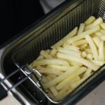 Close-up of raw french fries in a deep fryer basket ready for cooking.