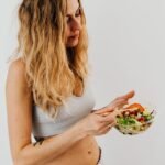 A caucasian woman in a sports bra enjoying a fresh salad, embodying healthy eating and lifestyle.