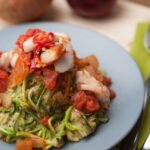 A plate of zucchini noodles topped with fresh tomato and fish, ideal for a healthy meal.