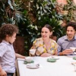 A family enjoys tea together in a beautiful indoor garden setting, surrounded by greenery.